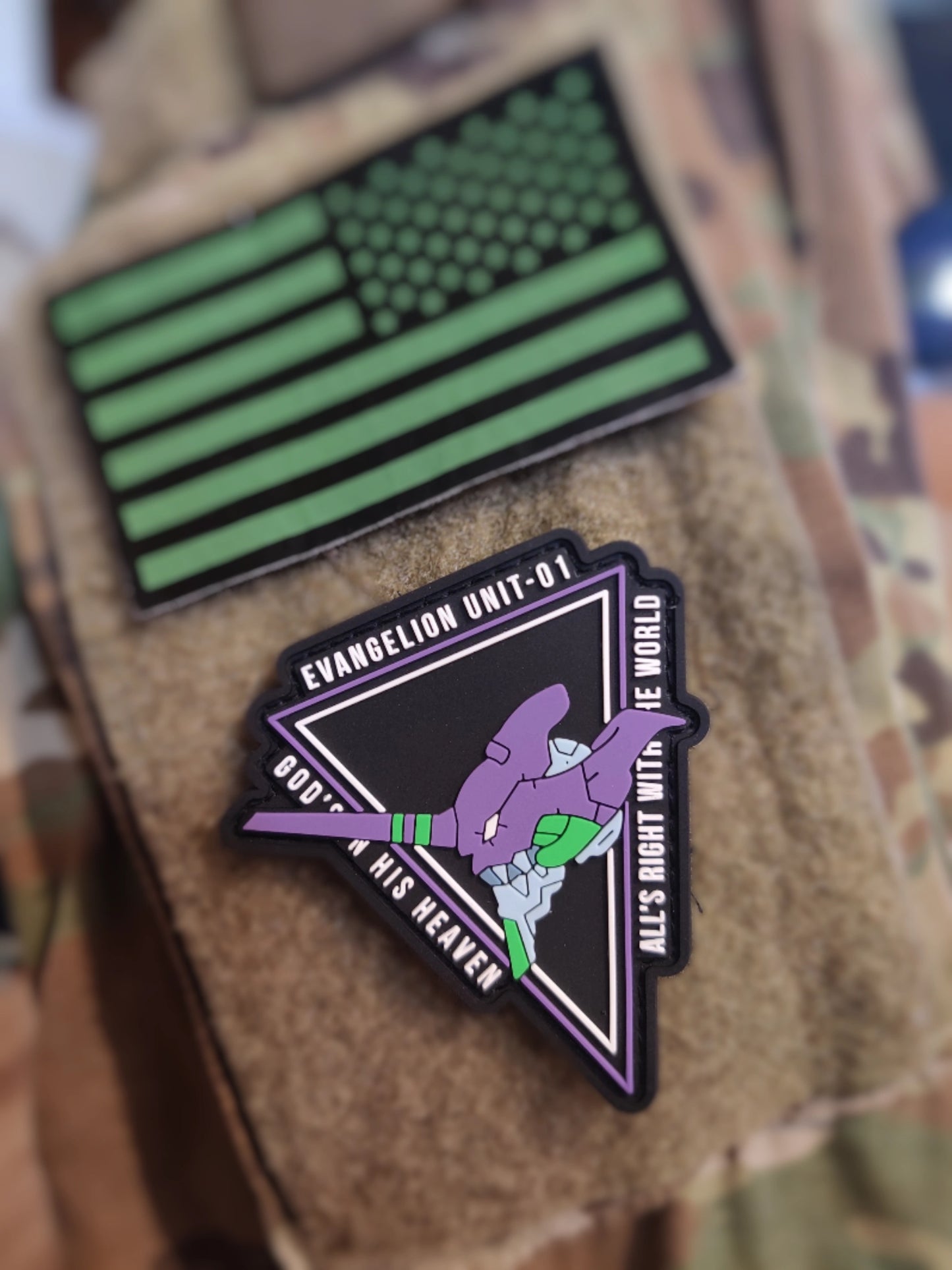 Two patches on a camouflage surface, one green American flag design and the other with a character and text.