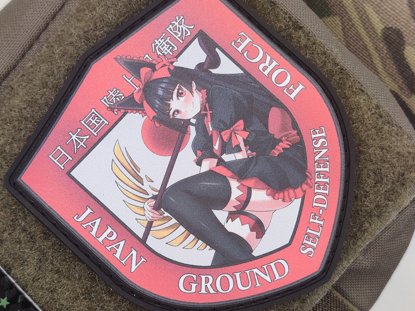 Patch with Rory Mercury from the anime Gate on a red background with the text Japan Ground Self-Defense Force on a military green texture surface