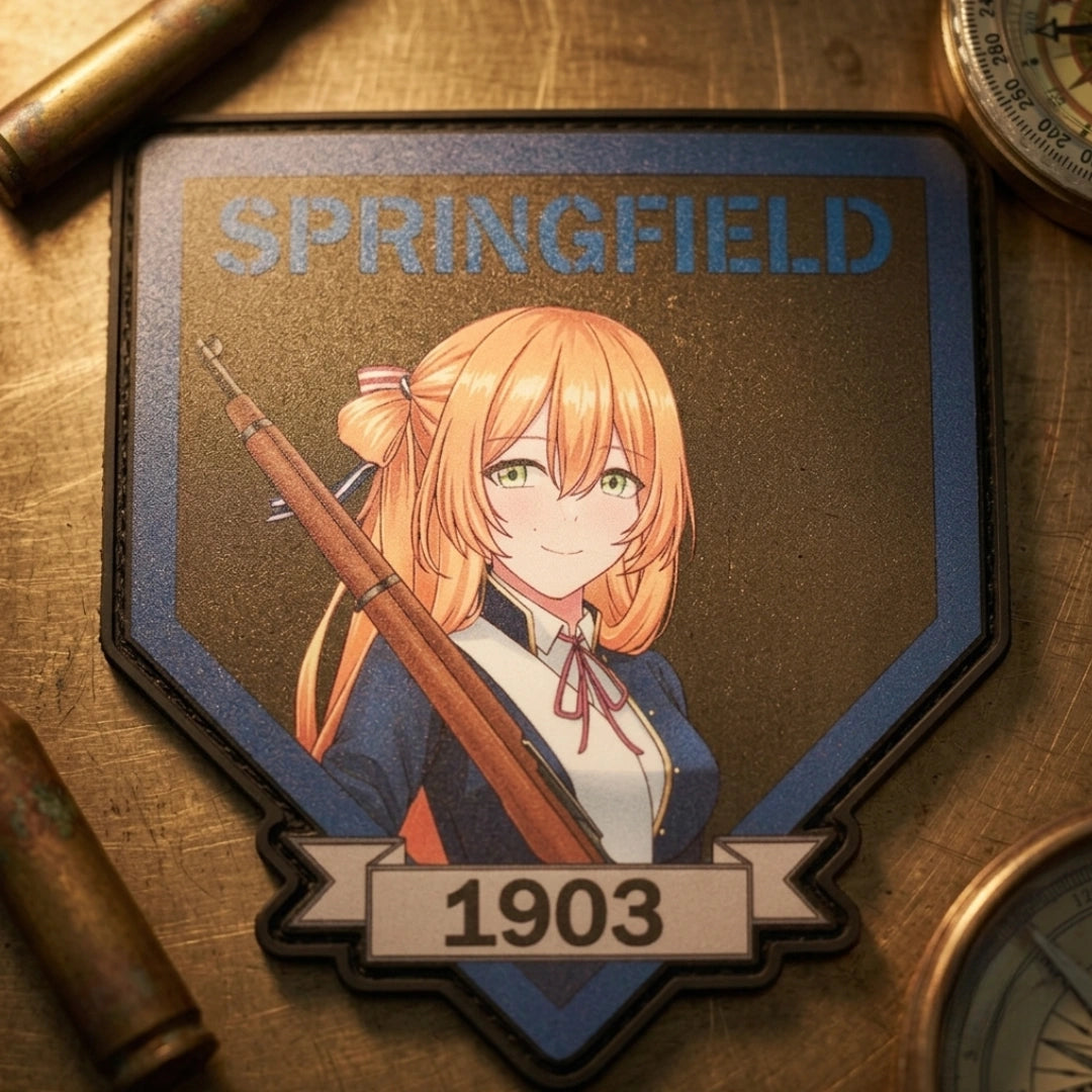 A shield-shaped embroidered patch featuring an anime-style orange-haired girl holding a rifle, with the text 'SPRINGFIELD' at the top and '1903' on a banner at the bottom, placed on a metallic surface with brass props around it.