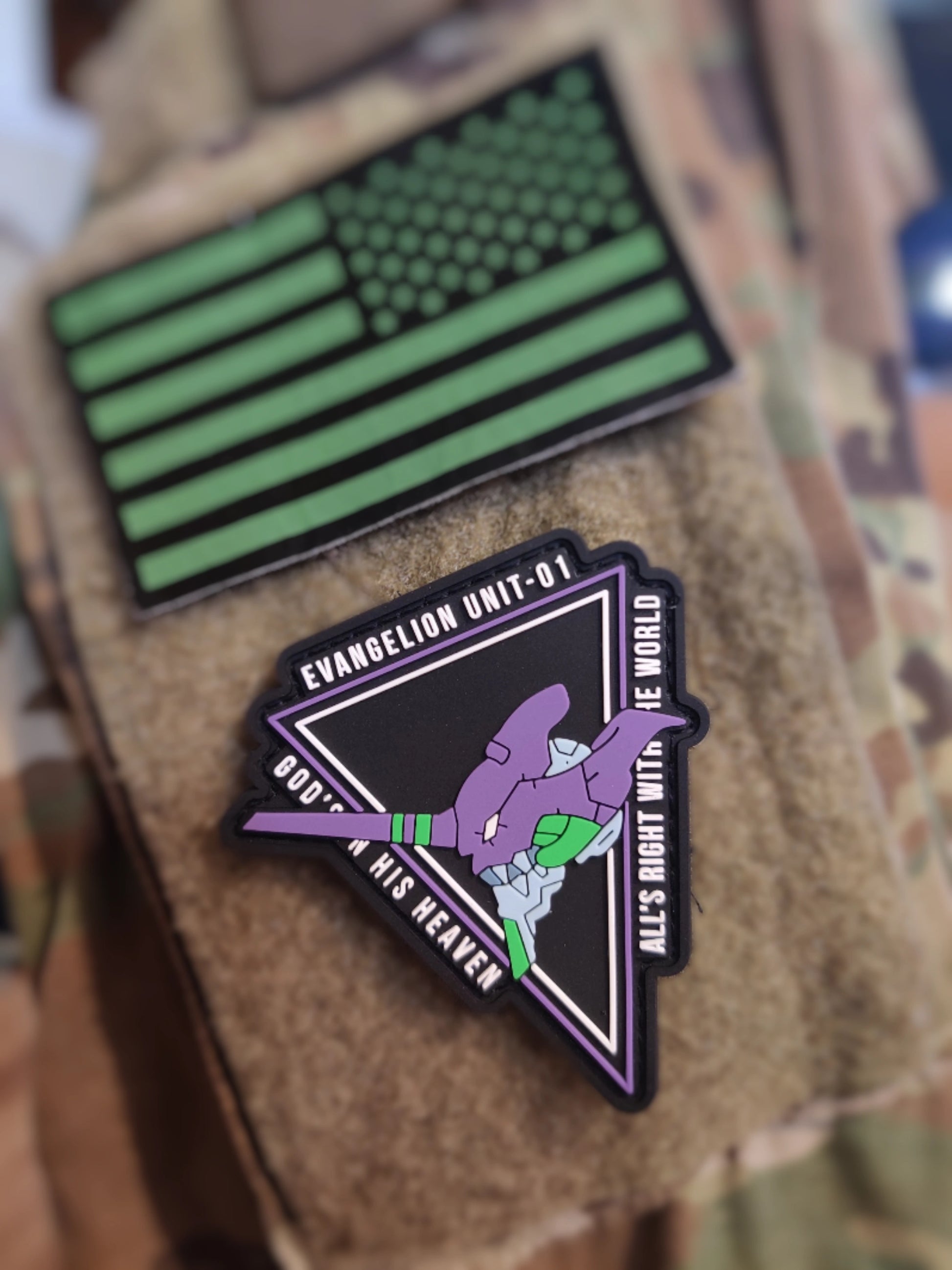 Two patches on a camouflage surface, one green American flag design and the other with a character and text.