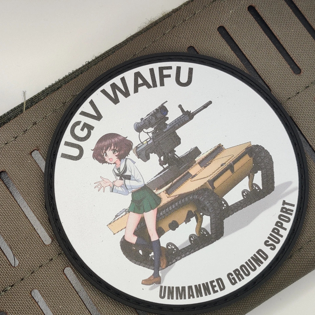 A circular patch featuring an anime-style illustration of a girl standing next to a tan unmanned ground support vehicle, with the text 'UGV WAIFU' and 'UNMANNED GROUND SUPPORT' on a white background.