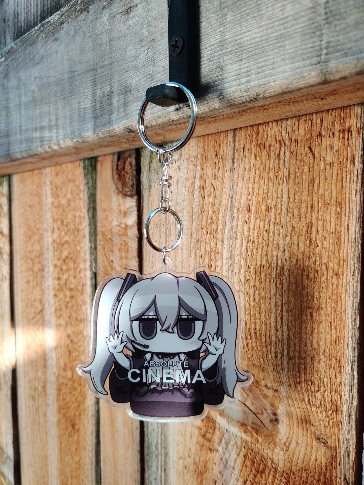 Keychain with anime character Hatsune Miku wearing a 'Absolute Cinema' shirt on a wooden background