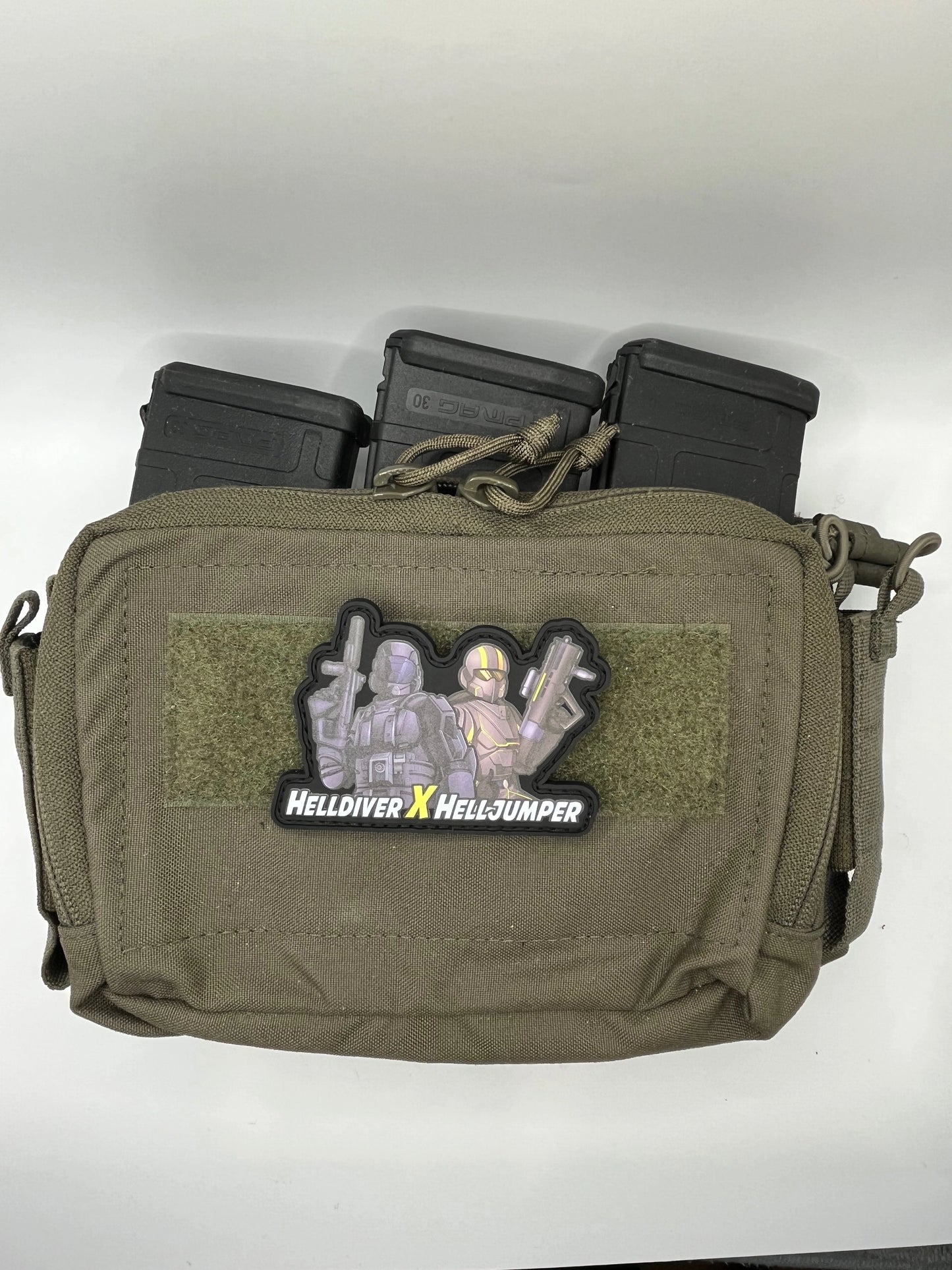 Olive green tactical pouch with 'Helldiver x Helljumper' patch and three black magazines on a white background.