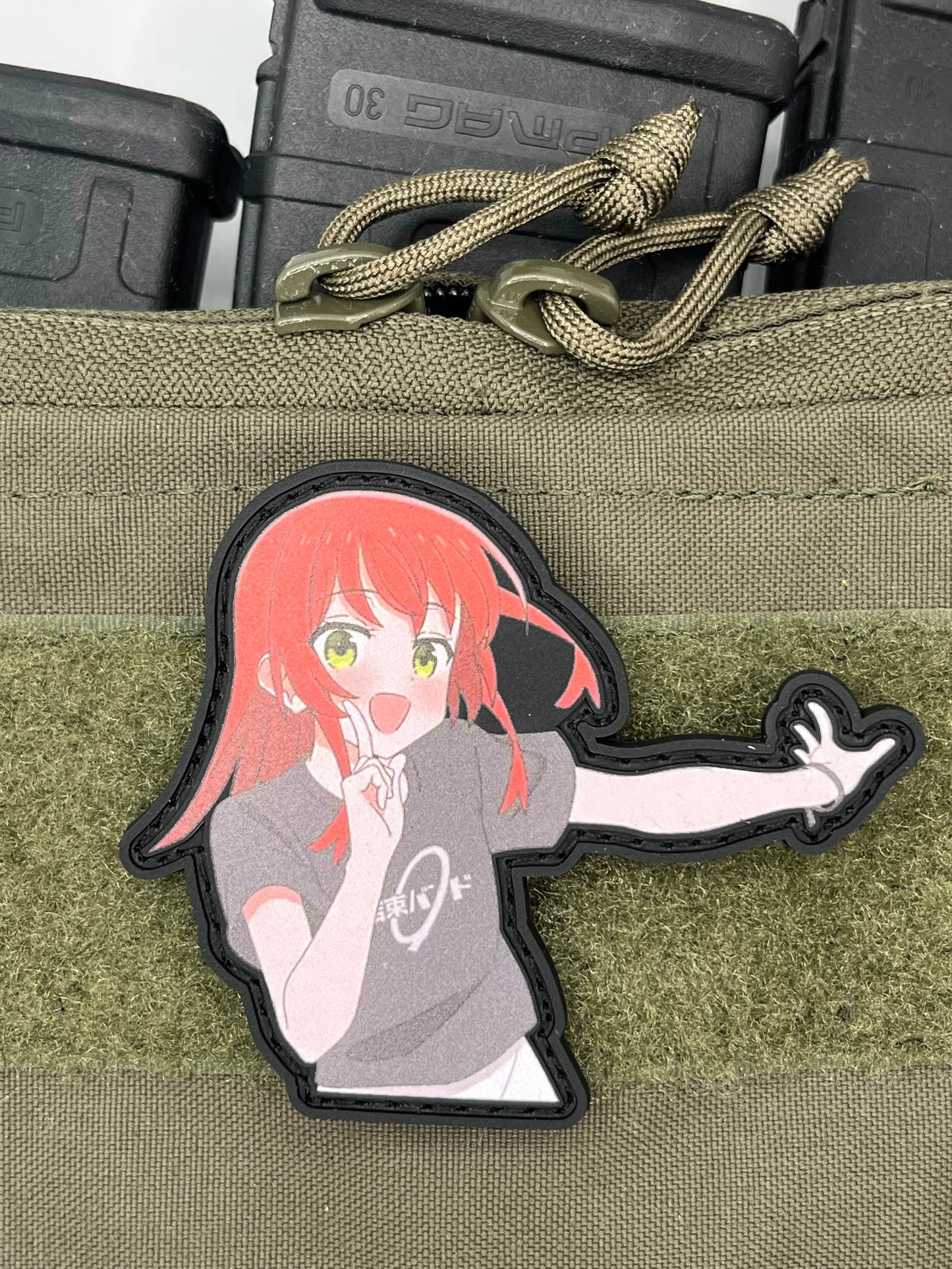 Anime character patch on a green tactical pouch with a brand logo.