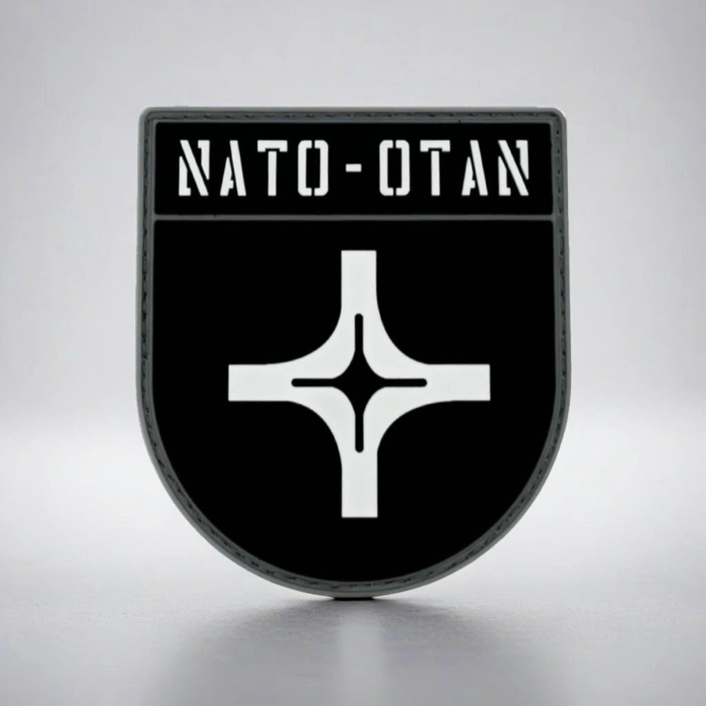 NATO logo on a black shield-shaped patch with a white border against a gray background