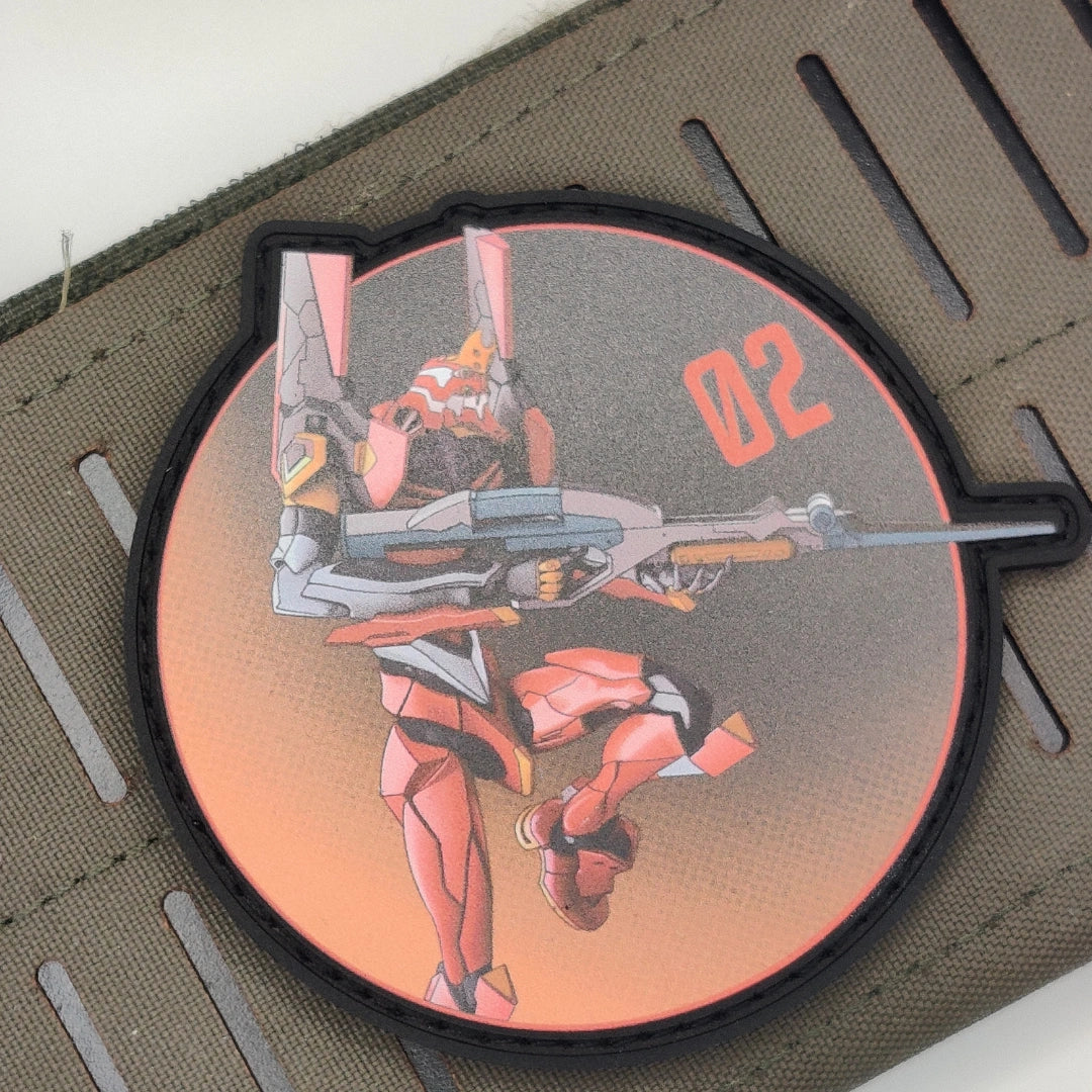 A circular tactical patch featuring an anime-style mecha robot in red, orange, and gray, with the number '02' in orange, shown on a textured olive drab strap.
