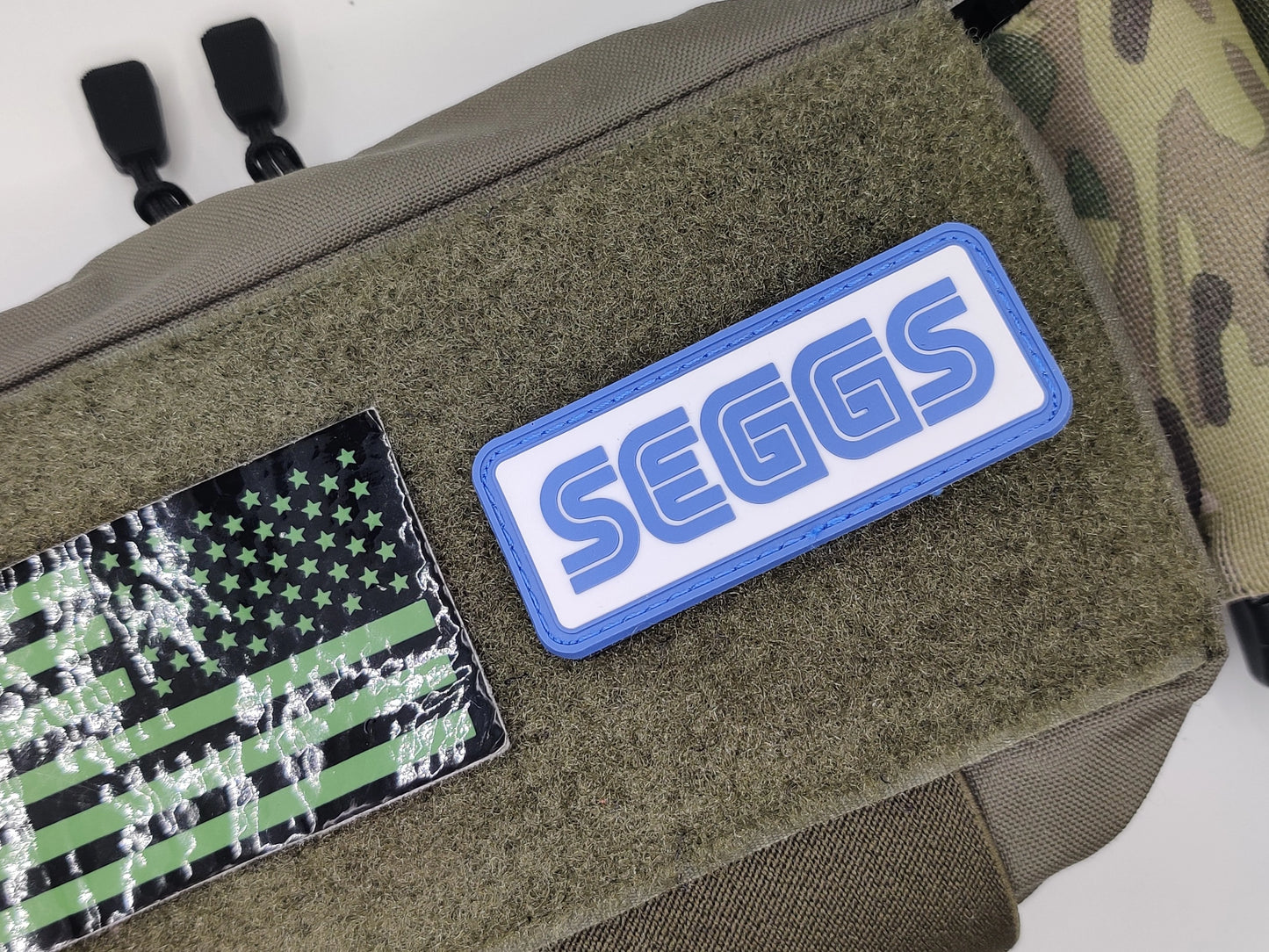 Patches on a green bag, including an American flag patch and a 'SEGGS' patch.