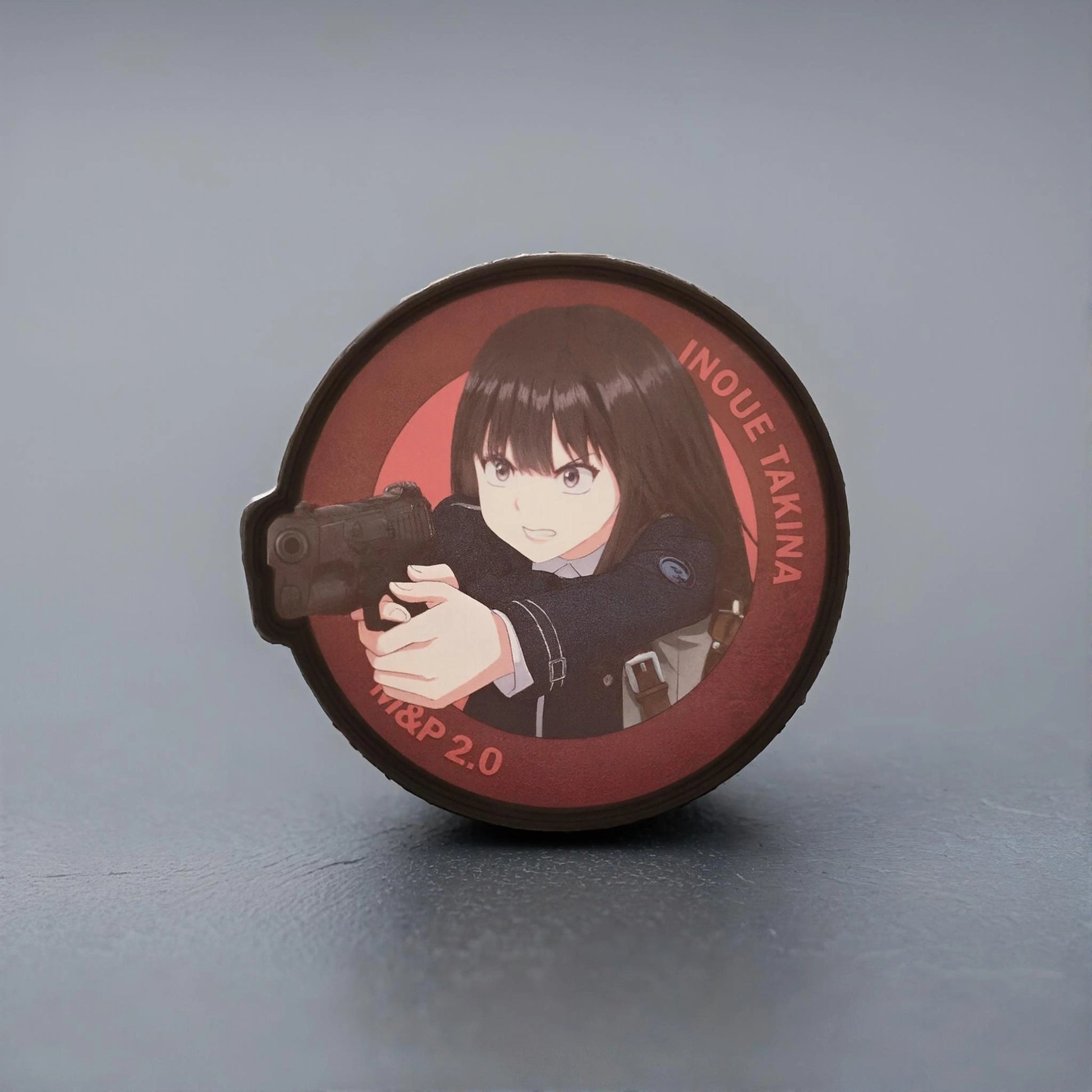 Circular product with an illustration of Takina Inoue from the anime Lycoris Recoil holding a gun on a gray background