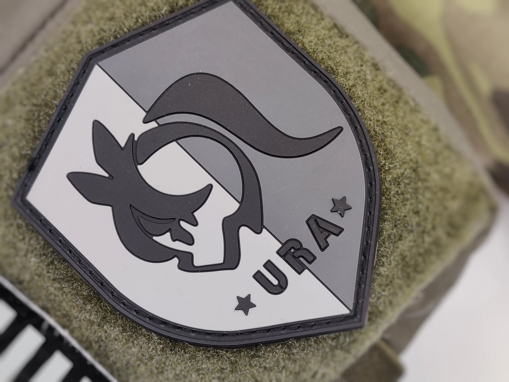 Shield-shaped logo with Umamusume Racing Association emblem and 'URA' text on a green texture background
