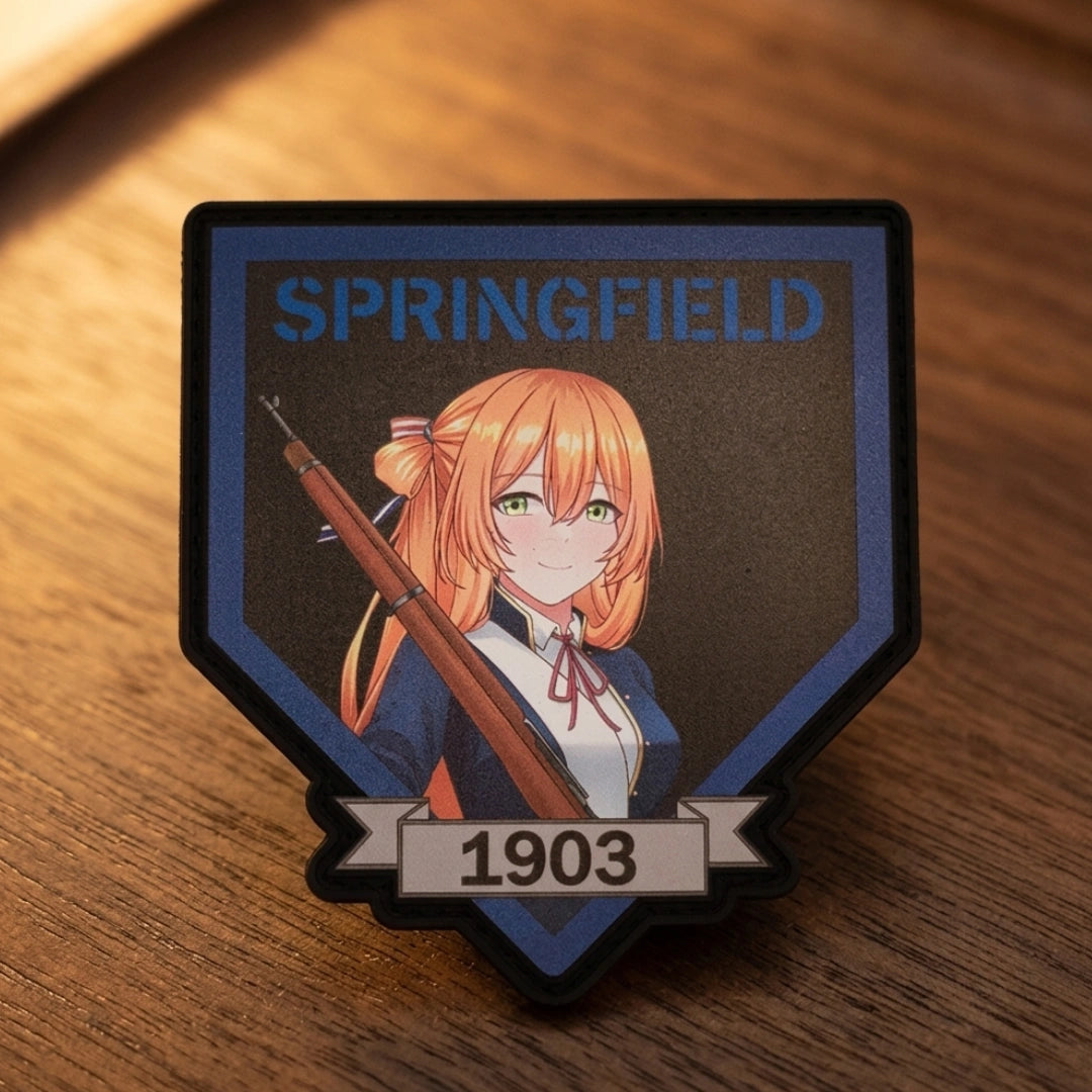 A shield-shaped enamel pin featuring an anime-style illustration of a girl with orange hair holding a rifle, with the text 'SPRINGFIELD' at the top and '1903' on a banner at the bottom, resting on a wooden surface.