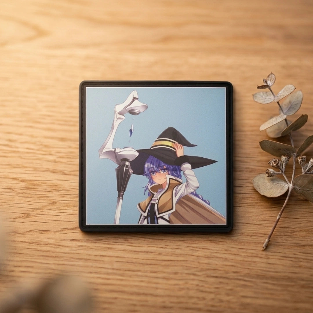 A square black-framed art print featuring an anime-style character with purple hair and a witch hat, displayed on a light wood tabletop next to dried eucalyptus stems.