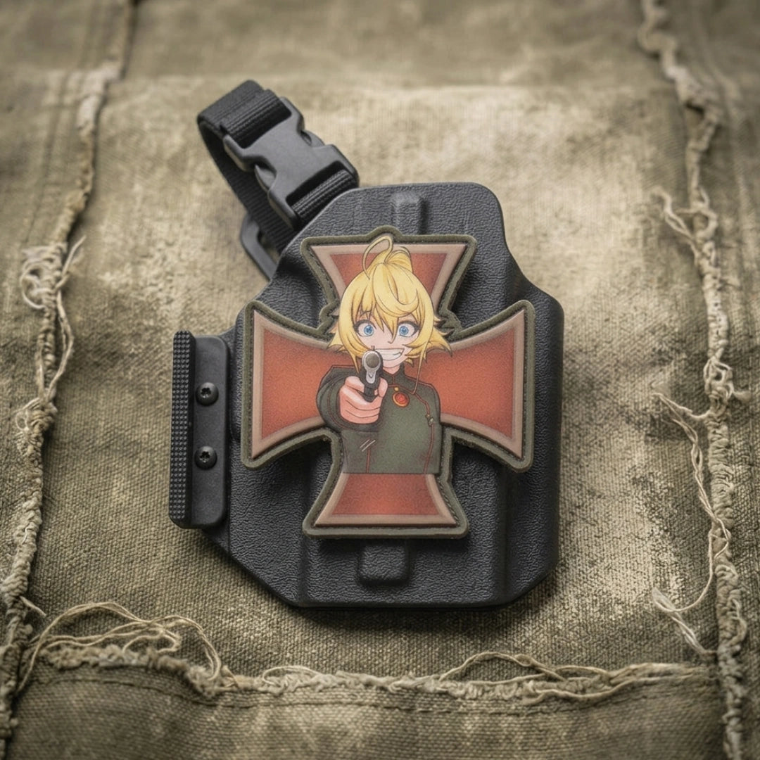A tactical PVC patch featuring an anime-style blonde character pointing a gun, mounted on a black Iron Cross-shaped background, displayed on a textured khaki canvas surface.